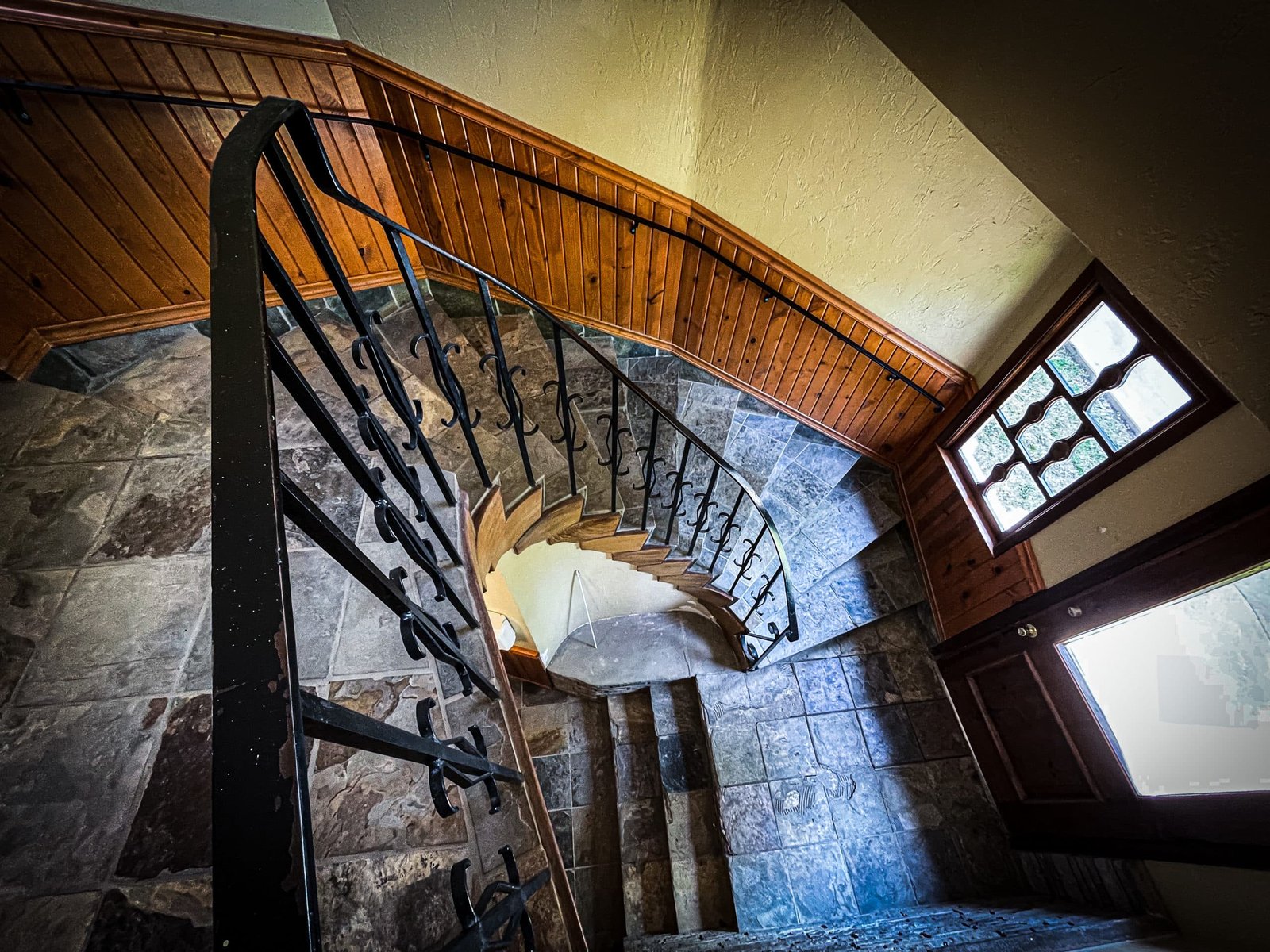 Spiral staircase with wooden railing and stone flooring leading to a window, showcasing the interior design of Blue Spruce Lodge.