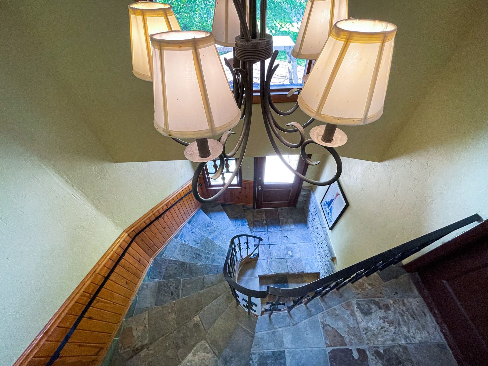 Staircase with stone steps and wooden railing, illuminated by a chandelier, leading to the entrance of the Blue Spruce Lodge.
