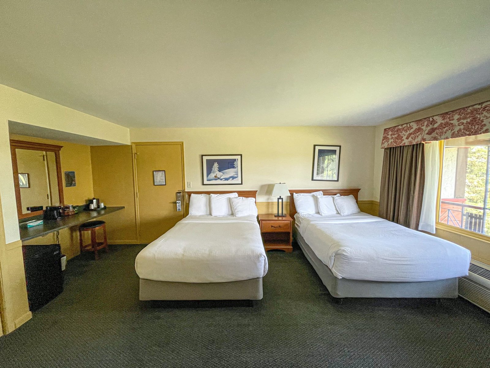 Hotel room at Blue Spruce Lodge featuring two double beds, a sitting area with a table, and amenities including a flat-screen TV and coffee station.
