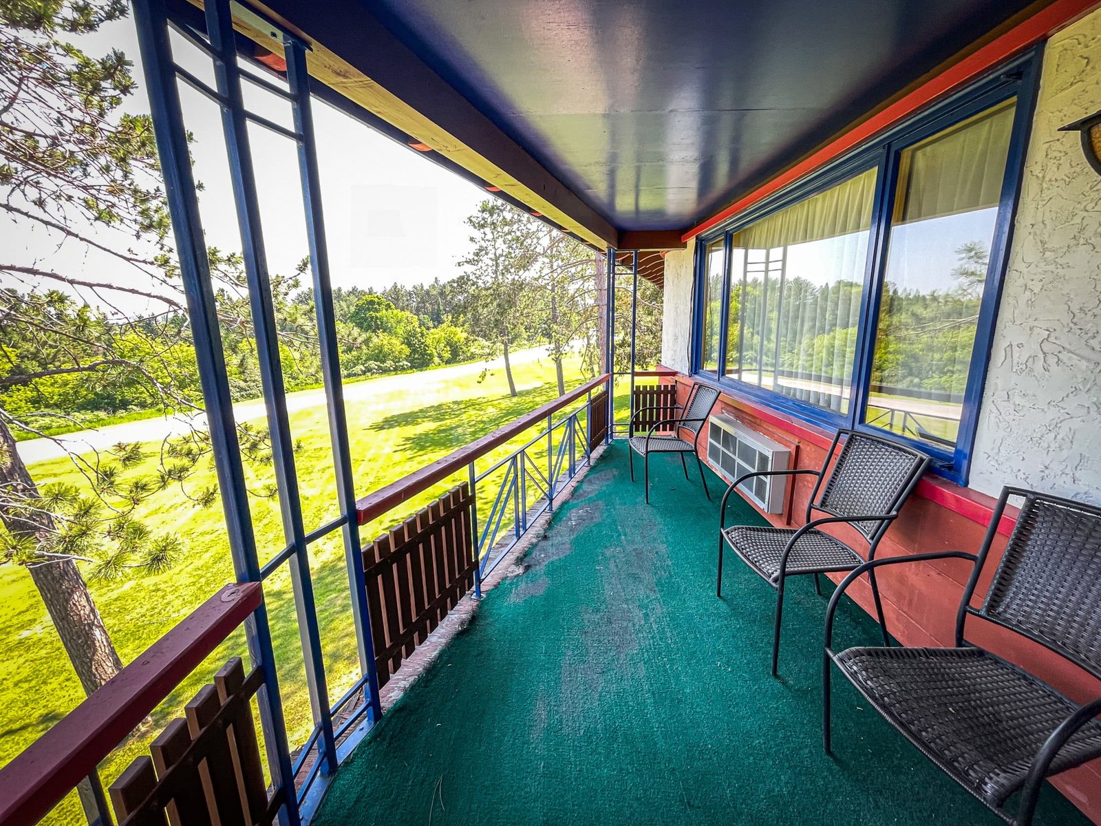 Balcony view of Blue Spruce Lodge with seating area, overlooking green landscape and trees.