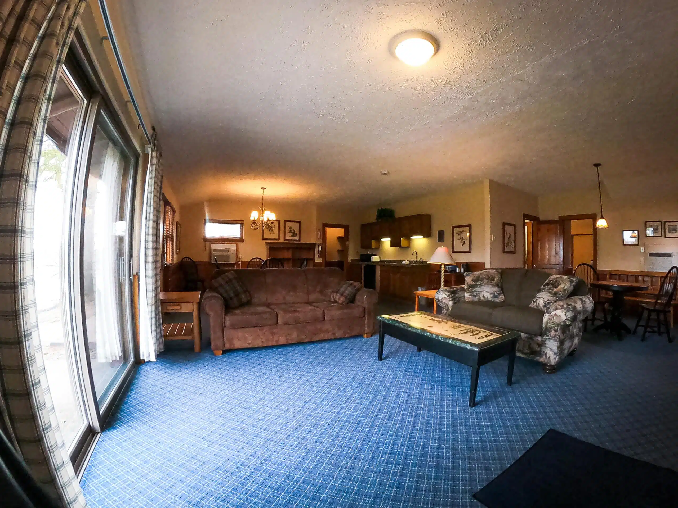 Spacious living area of a 2 bedroom chalet at Otsego Resort, featuring a sofa, kitchenette, dining area, and large windows with natural light.