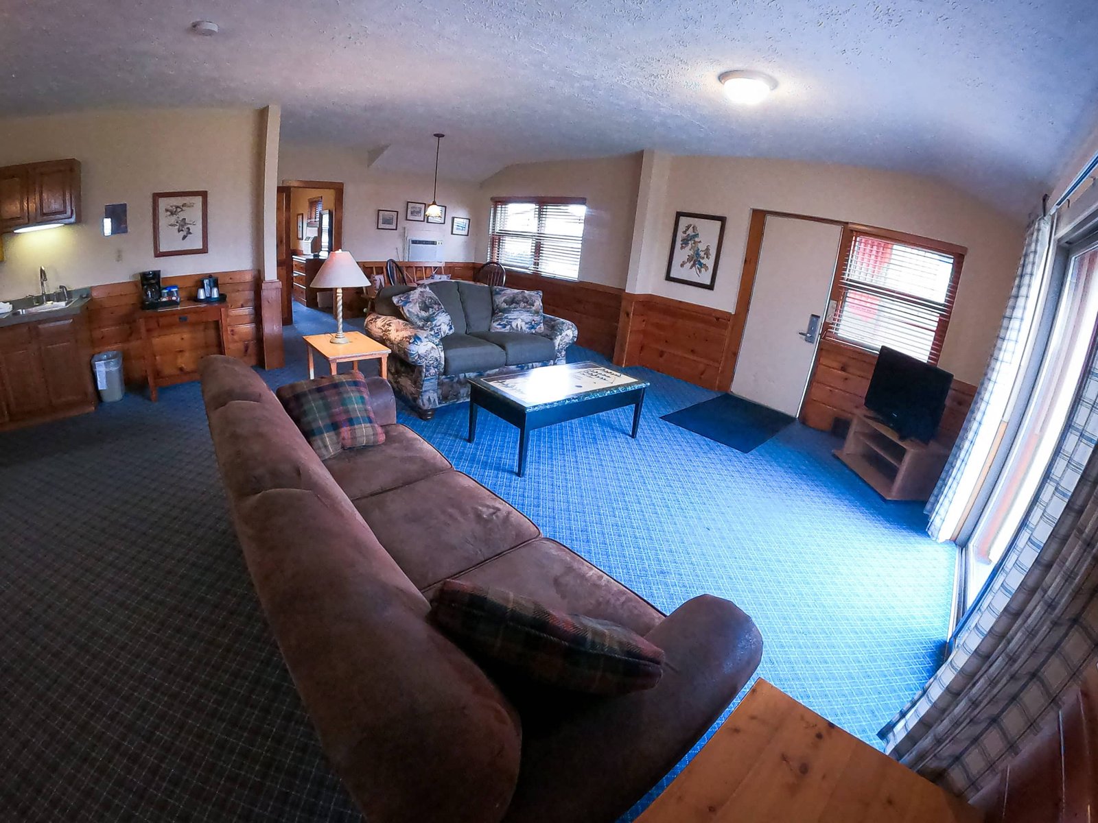 Spacious living room of a chalet at Otsego Resort featuring a sofa, armchair, coffee table, kitchenette, and flat-screen TV, designed for comfort and relaxation.
