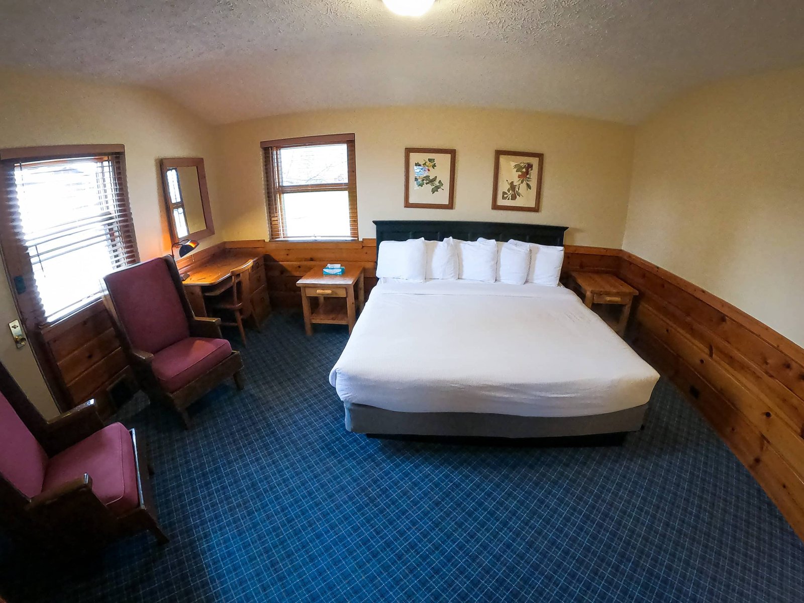Spacious chalet bedroom featuring a king-sized bed with multiple pillows, two wooden chairs, a desk, and large windows for natural light at Otsego Resort.