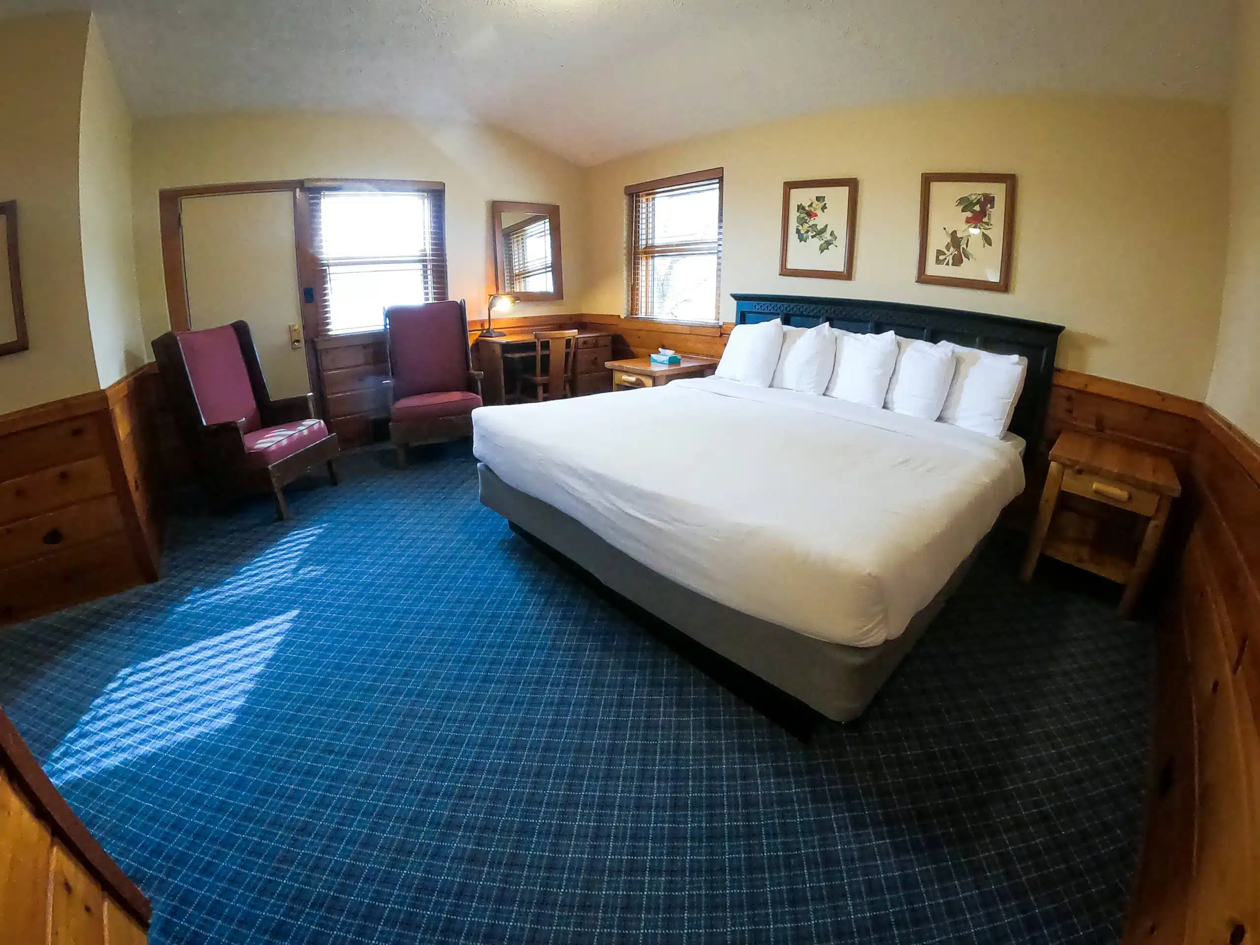 Spacious chalet bedroom with a king-sized bed, two armchairs, desk area, and wooden accents, showcasing a cozy and inviting atmosphere at Otsego Resort.