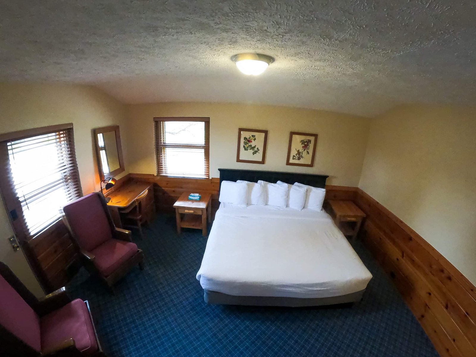 Spacious chalet bedroom with a large bed, two armchairs, wooden furniture, and natural light from windows, highlighting comfort and rustic decor at Otsego Resort.