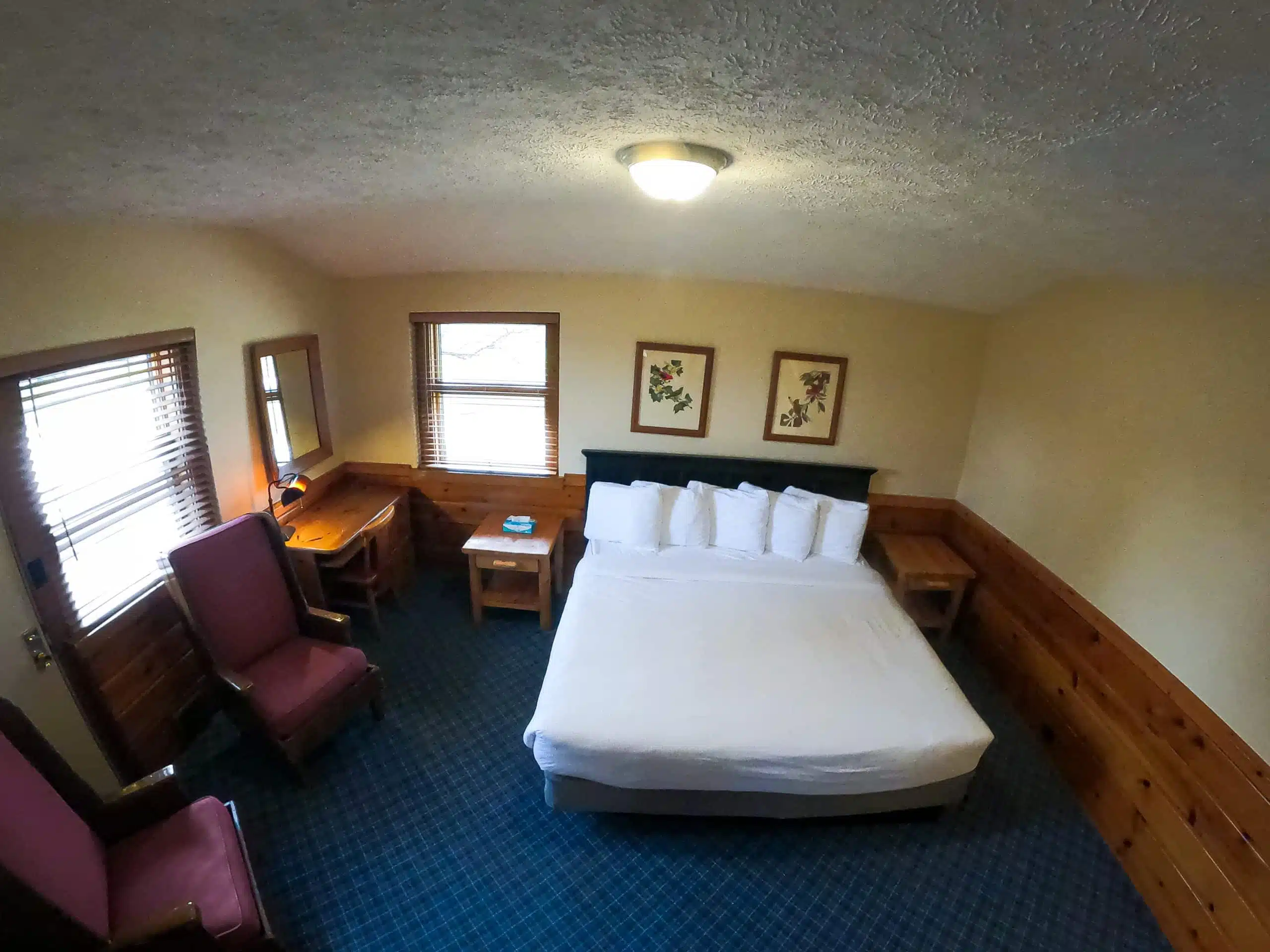 Spacious chalet bedroom with a large bed, two armchairs, wooden furniture, and natural light from windows, highlighting comfort and rustic decor at Otsego Resort.