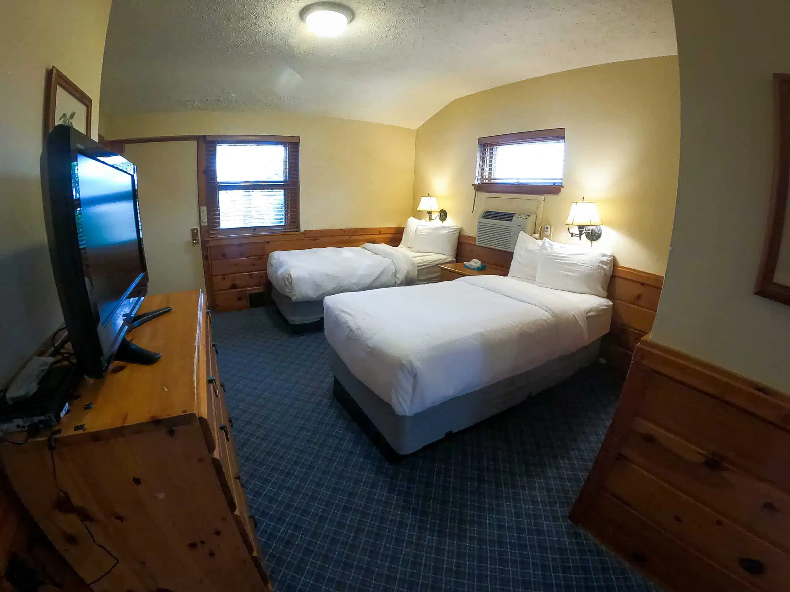 Spacious chalet bedroom with two beds, flat-screen TV, air conditioning, and wooden accents at Otsego Resort.
