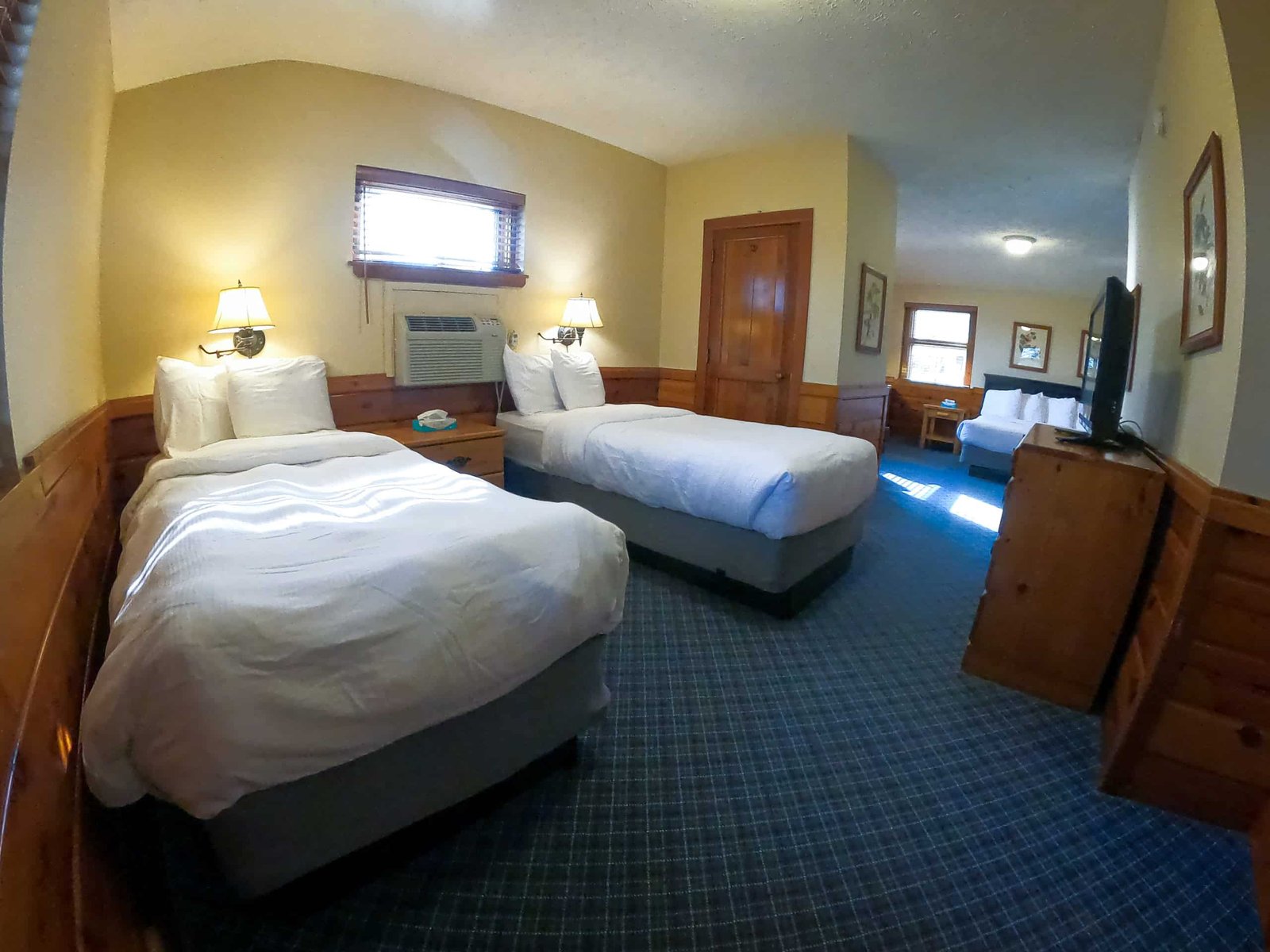 Spacious chalet room with two beds, wooden accents, air conditioning, and flat-screen TV, showcasing amenities for a comfortable stay at Otsego Resort.