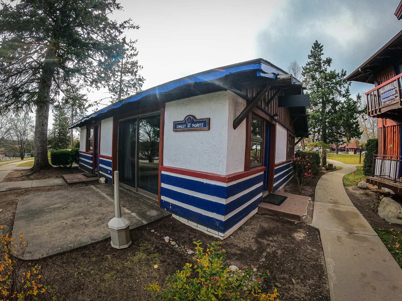 Chalet St. Moritz exterior with blue and white striped design, surrounded by greenery and a pathway, highlighting the Otsego Resort's chalet accommodations.