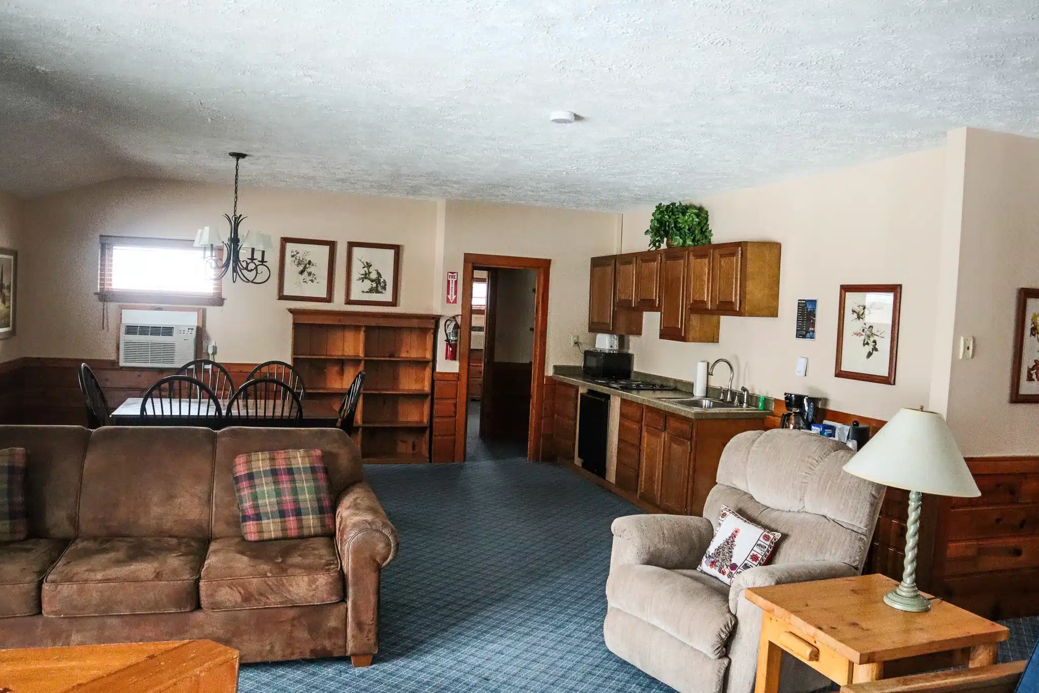 Spacious chalet interior featuring a living room with sofa, kitchenette, dining area, and rustic decor, ideal for accommodating 6-8 guests at Otsego Resort.