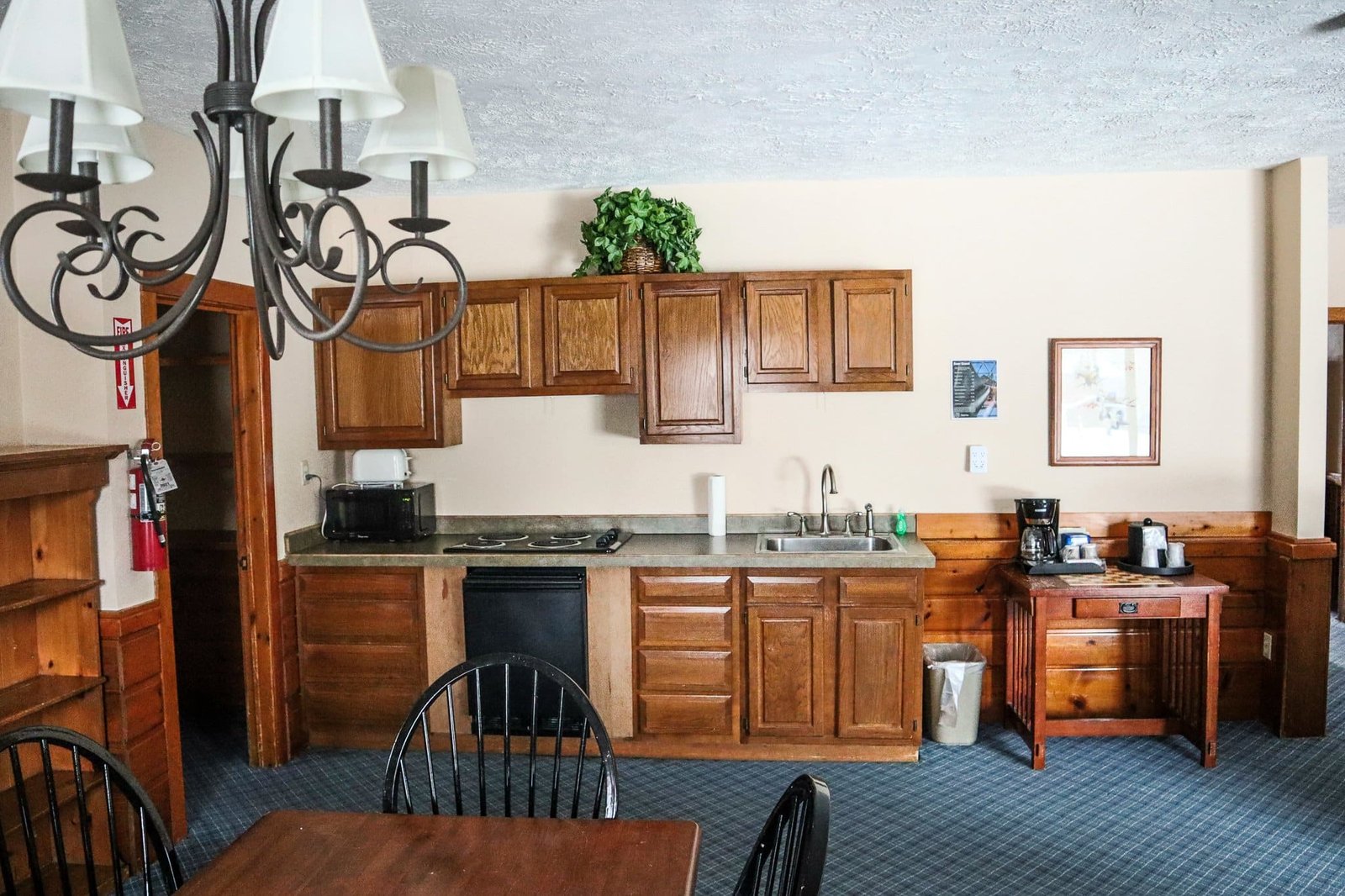 Chalet kitchenette featuring wooden cabinets, stovetop, microwave, coffee maker, and dining area with black chairs, reflecting the spacious accommodations at Otsego Resort.