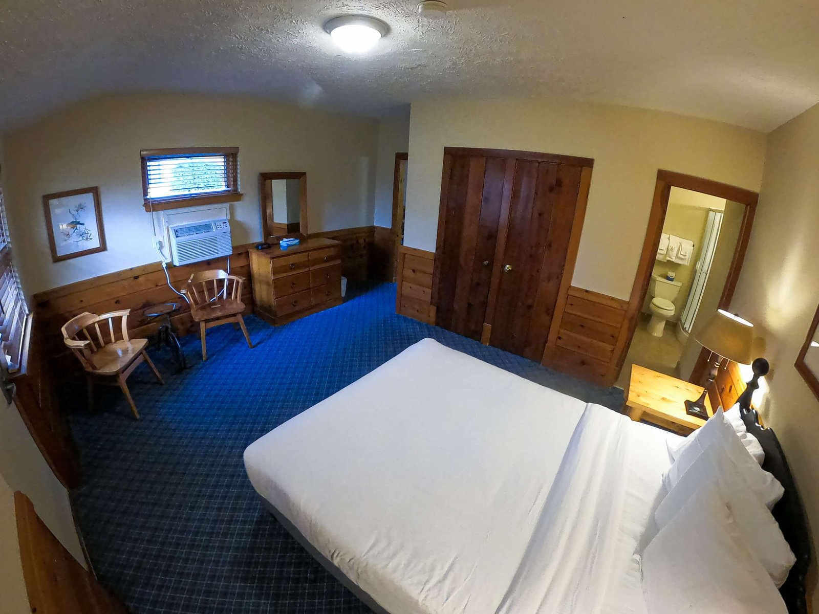 Spacious chalet interior featuring a queen bed, wooden furniture, air conditioning unit, and a bathroom visible through an open door, designed for comfort at Otsego Resort.