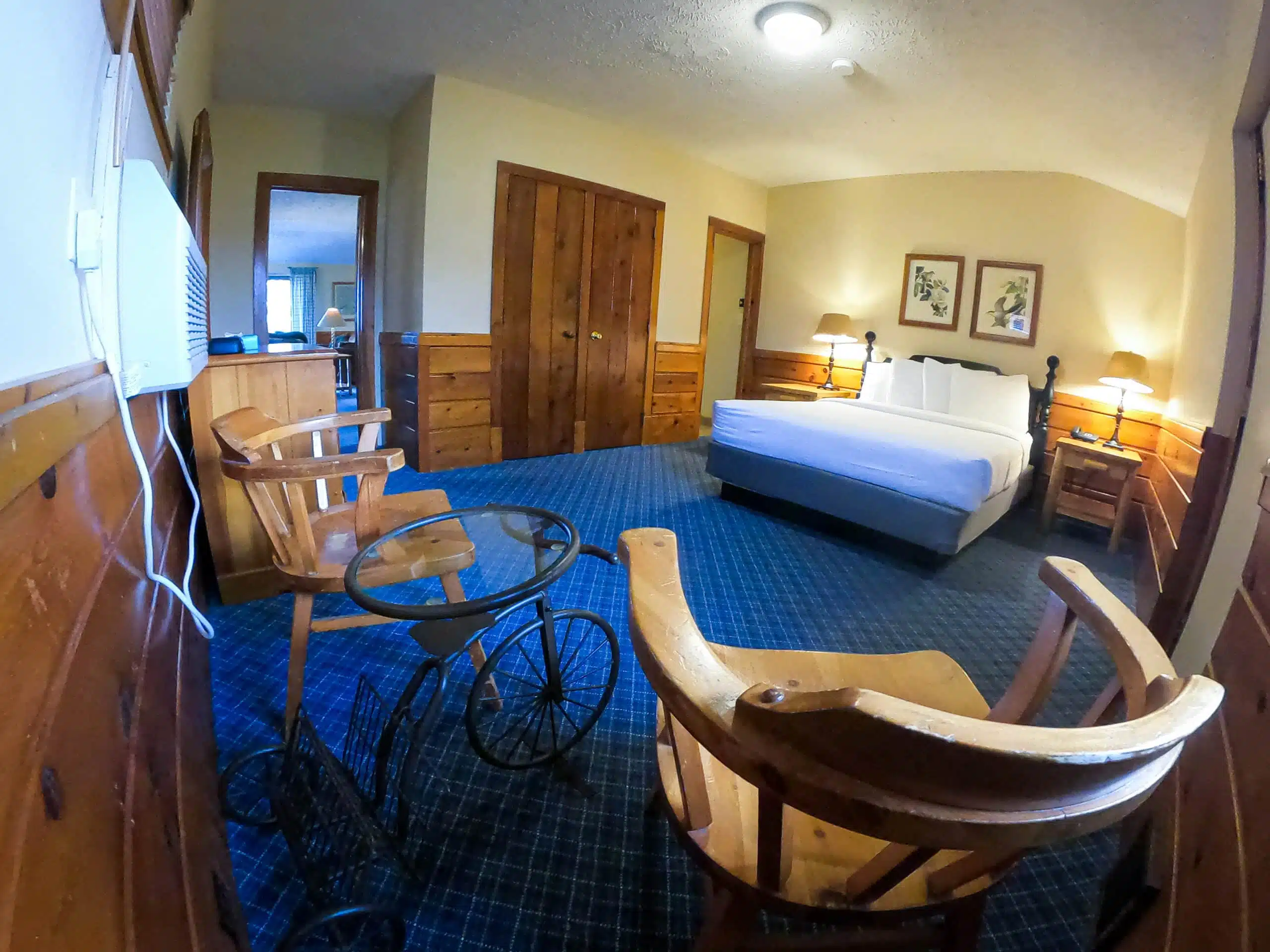 Spacious chalet interior featuring a king-sized bed, wooden furniture, seating area with chairs and glass table, and warm lighting, reflecting the cozy accommodations at Otsego Resort.