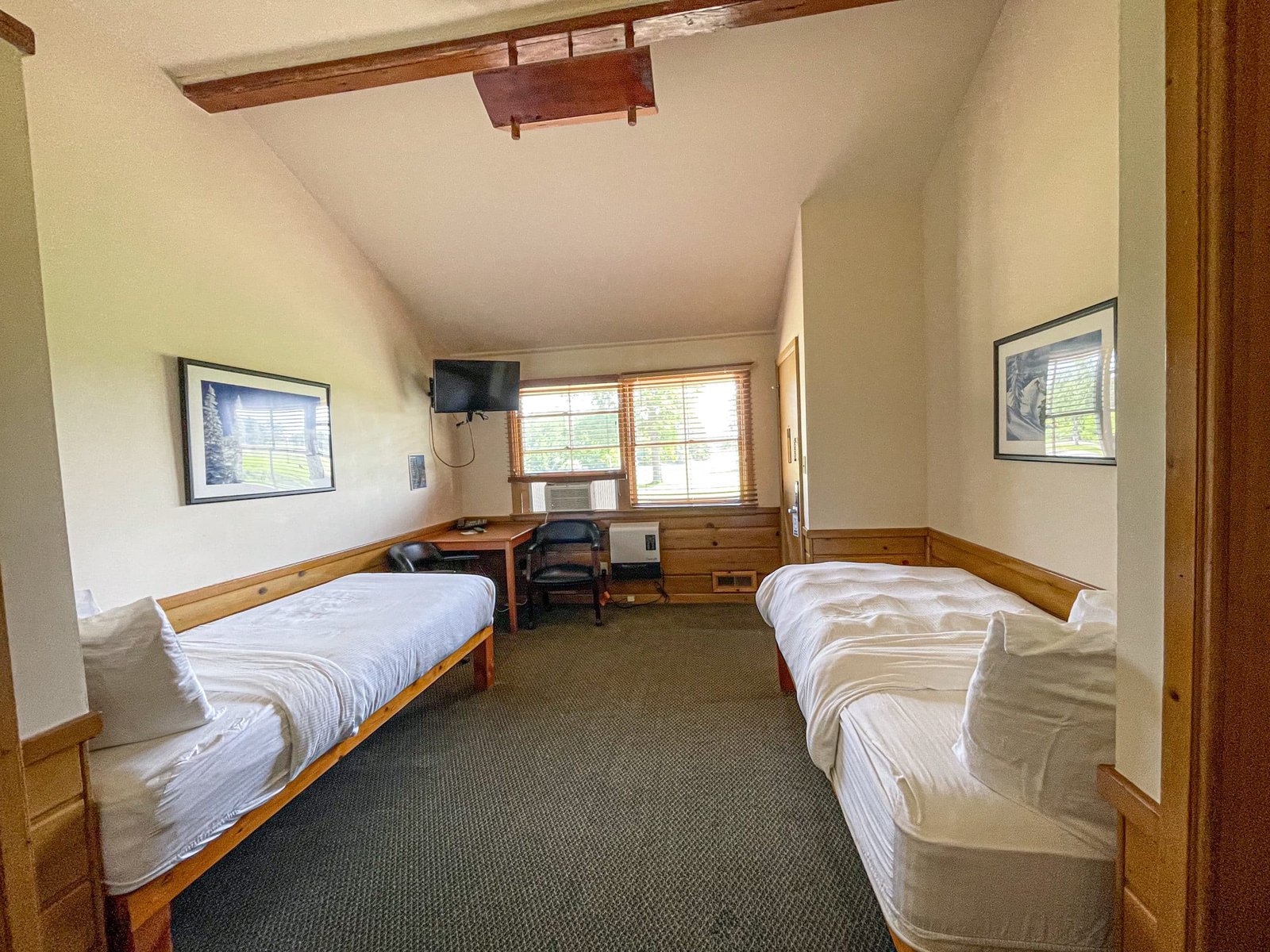Loft Lodge hotel room featuring two twin beds, workspace with table and chairs, flat-screen TV, and natural light from windows, highlighting northern Michigan's inviting atmosphere.