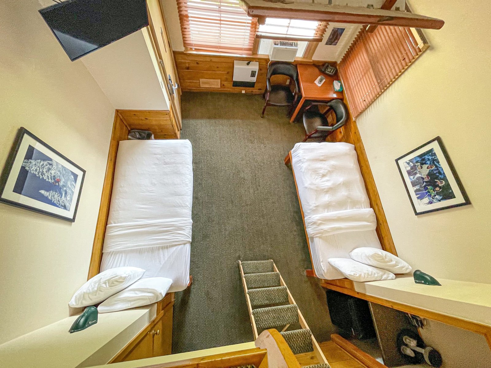 Loft Lodge hotel room at Otsego Resort featuring two twin beds, workspace with table and chairs, flat-screen TV, and decorative wall art, showcasing northern Michigan's cozy accommodations.