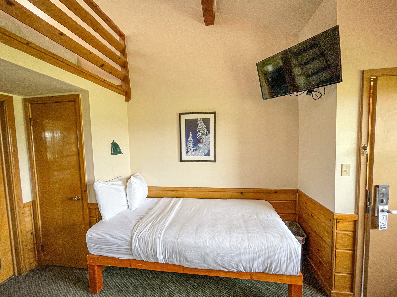 Cozy hotel room at the Loft Lodge featuring a twin bed, flat-screen TV, wooden accents, and a serene mountain-themed artwork, designed for comfort and convenience in northern Michigan.