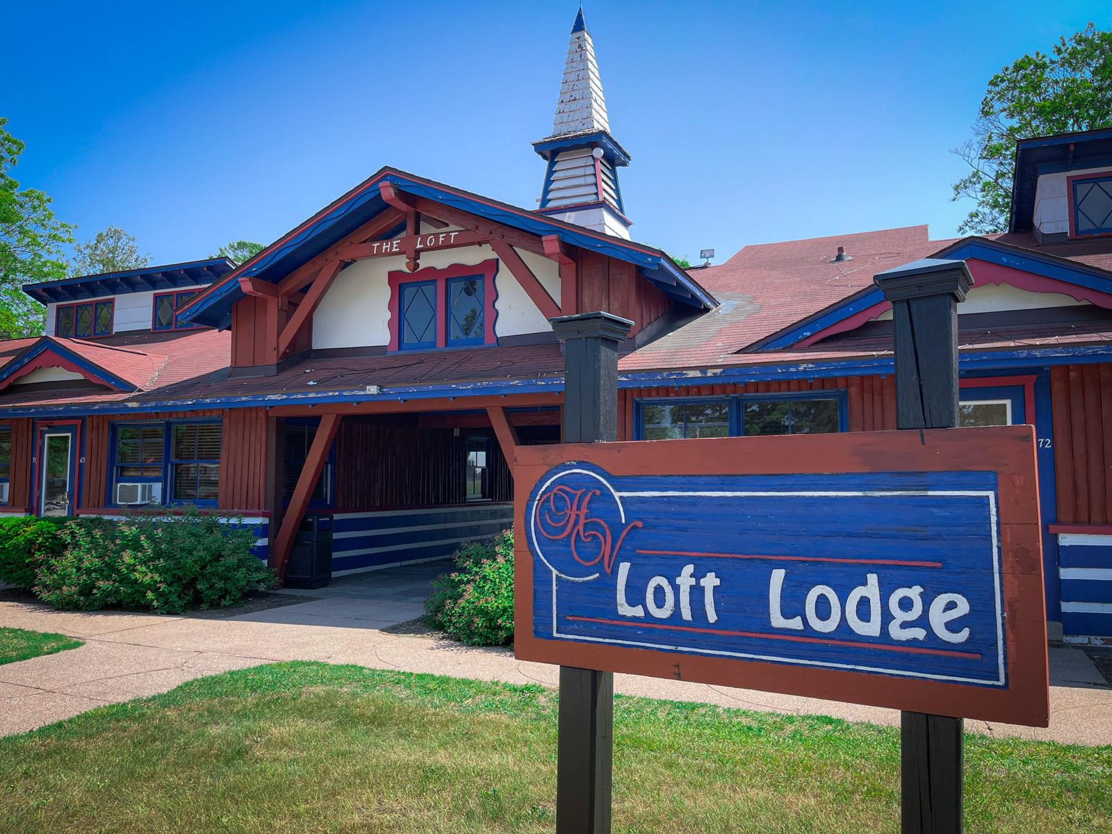 Loft Lodge exterior at Otsego Resort featuring colorful architectural details, welcoming sign, and lush greenery, highlighting accommodations in northern Michigan.
