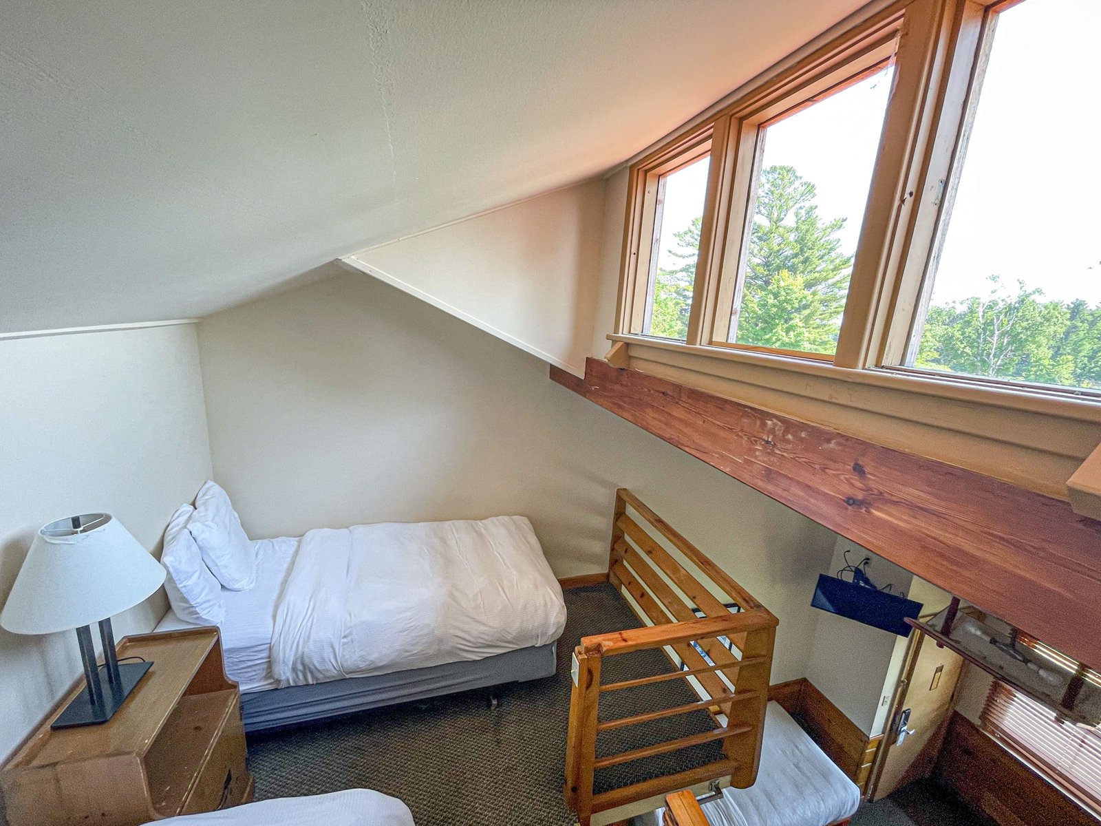 Cozy hotel room at the Loft Lodge featuring two twin beds, wooden accents, a bedside lamp, and large windows offering views of northern Michigan's landscape.