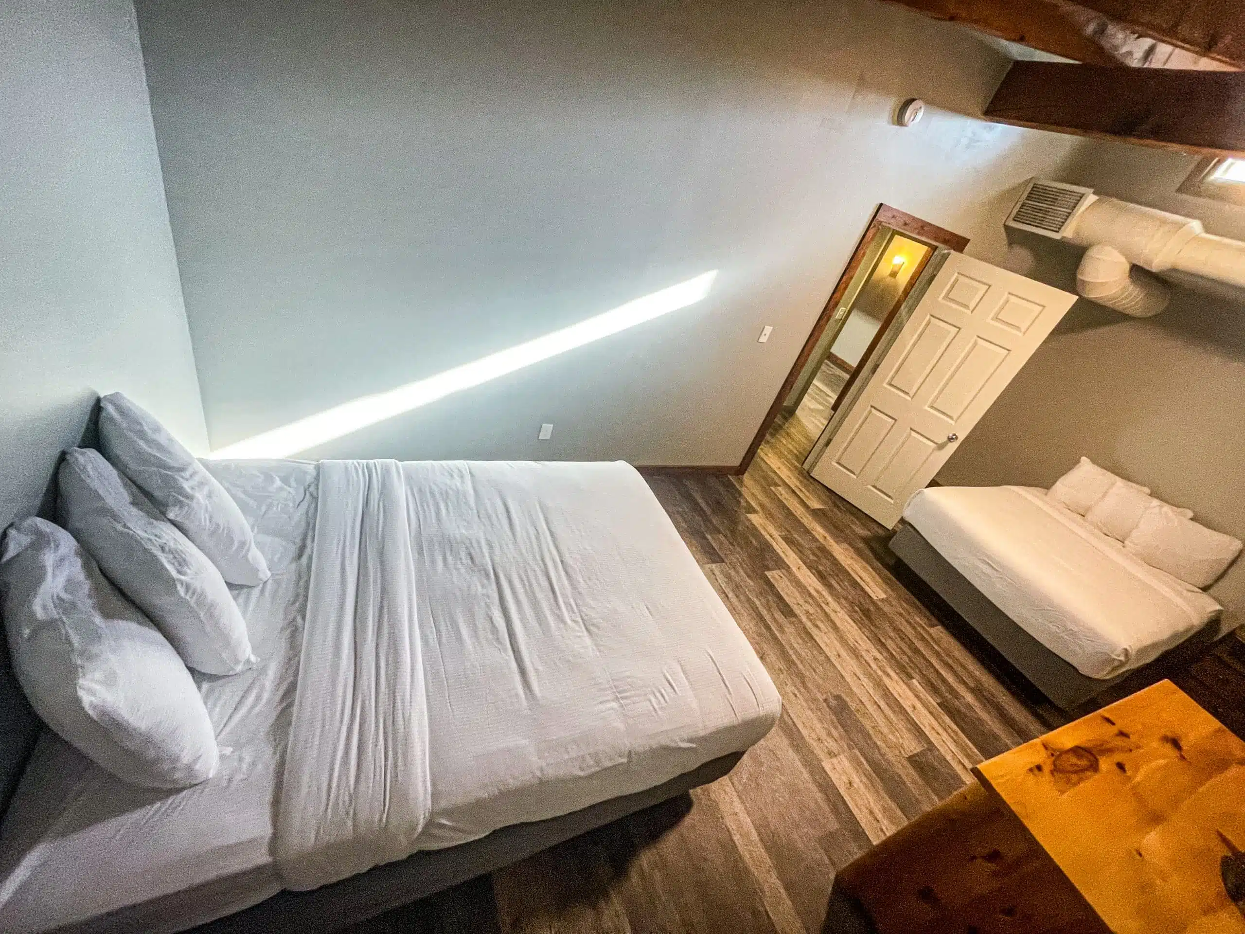Interior view of a bedroom in the Classic Lodge at Otsego Resort, featuring a large bed with white linens, a smaller bed, wooden furniture, and natural light streaming through a window.