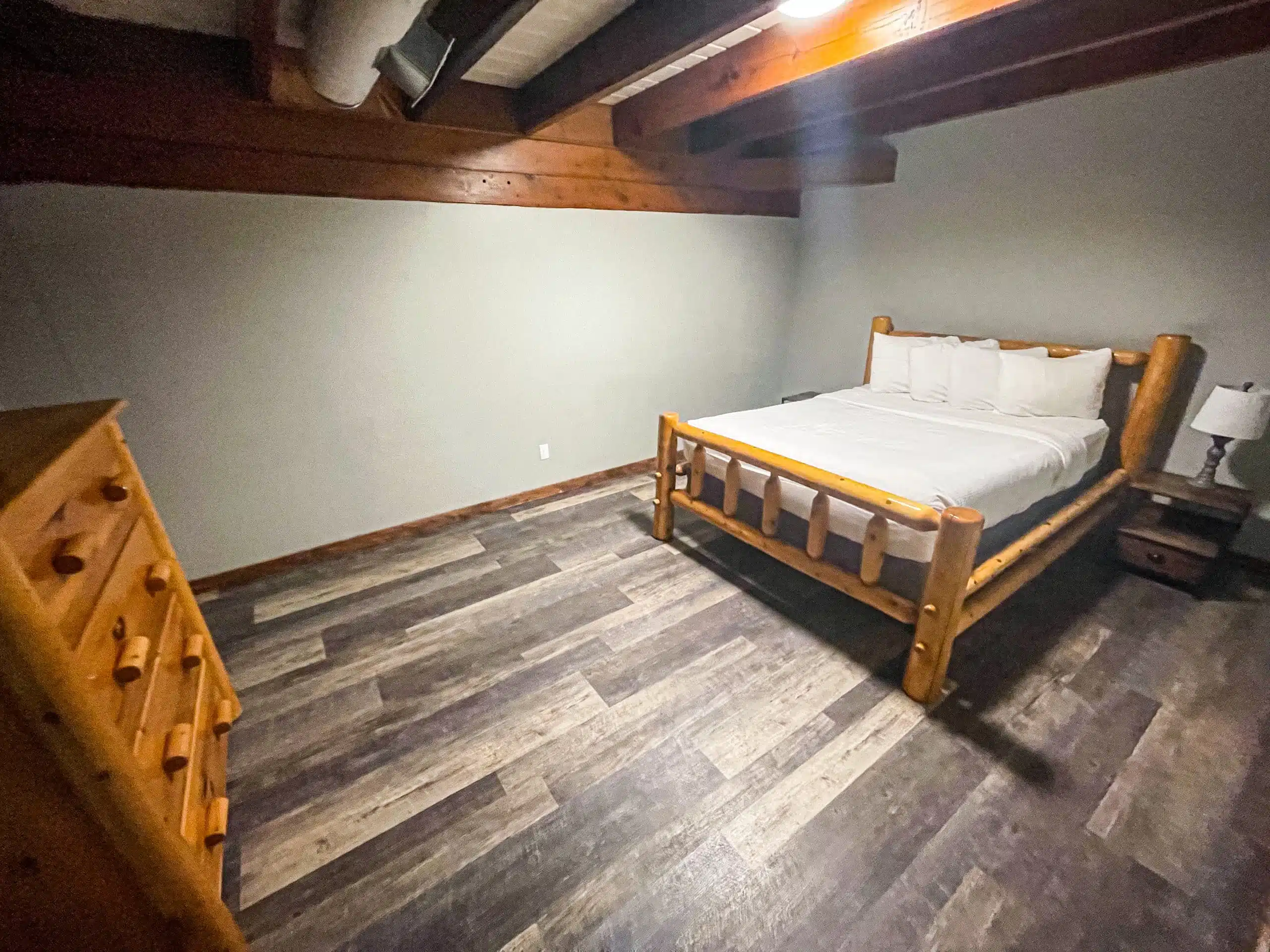 Cozy bedroom in The Classic Lodge at Otsego Resort featuring a log-style bed, wooden dresser, and rustic decor, emphasizing comfort and relaxation for guests.