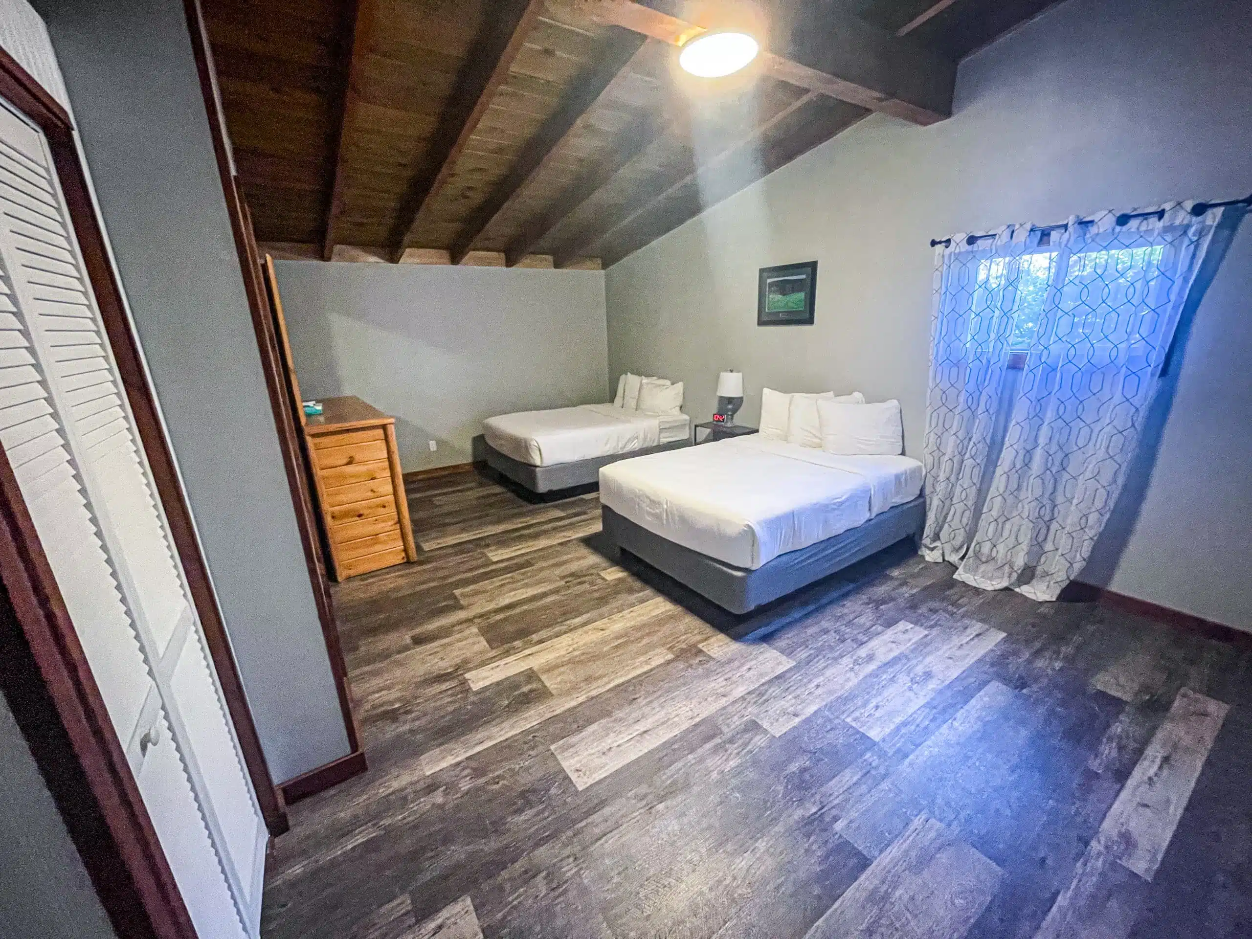 Spacious bedroom in the Classic Lodge at Otsego Resort featuring two double beds, wooden furniture, and large windows with natural light.