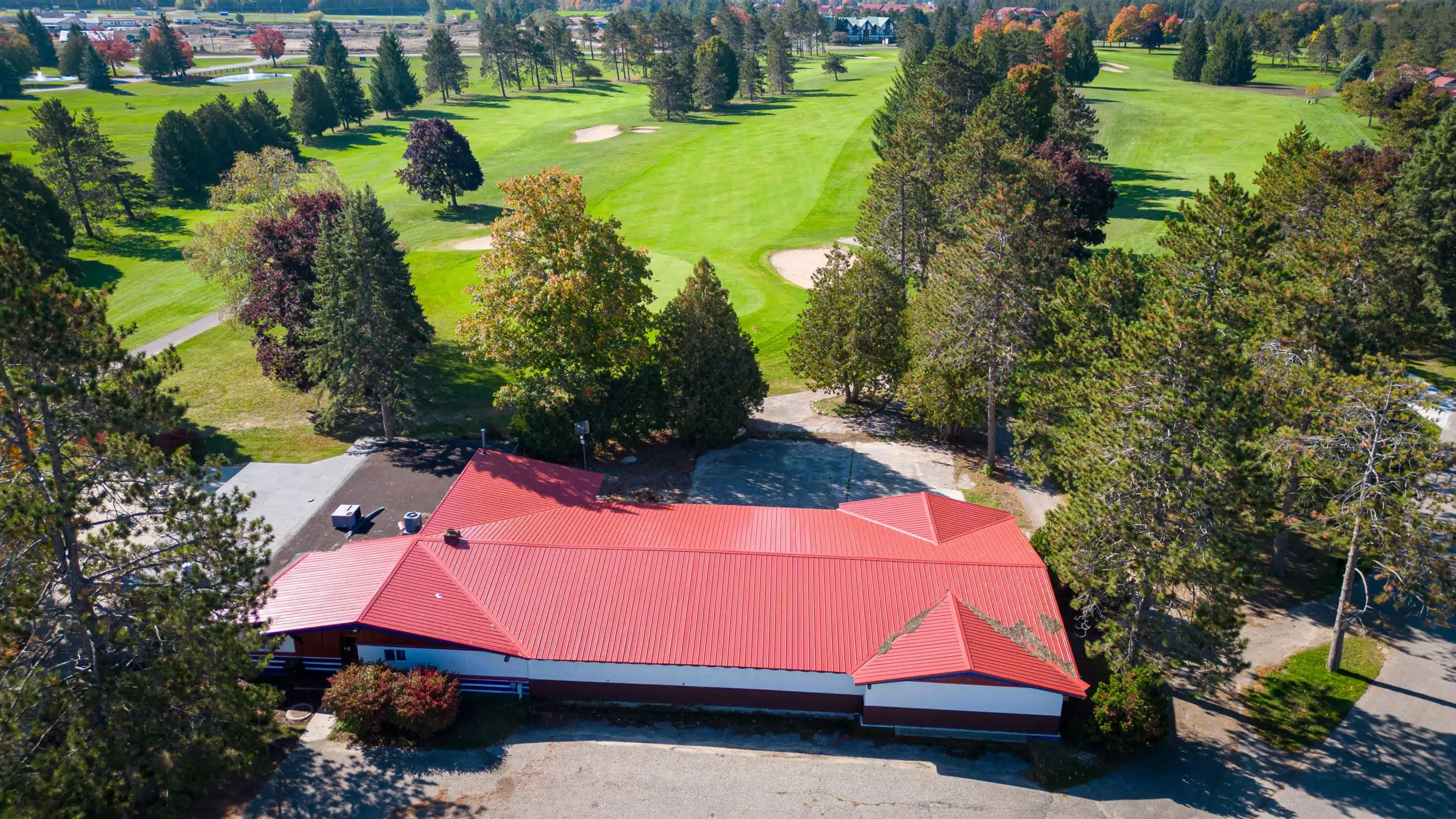 Aerial view of the Classic Lodge at Otsego Resort, featuring a red-roofed building surrounded by lush green golf course, trees, and pathways, highlighting its prime location on the 18th hole.
