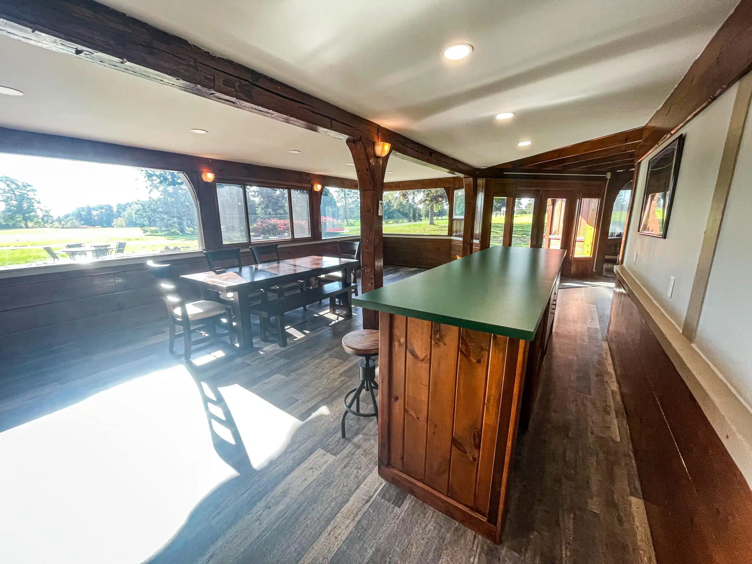 Interior view of the Classic Lodge at Otsego Resort, featuring a large dining table, bar area with green countertop, and large windows overlooking the 18th hole of The Classic golf course.