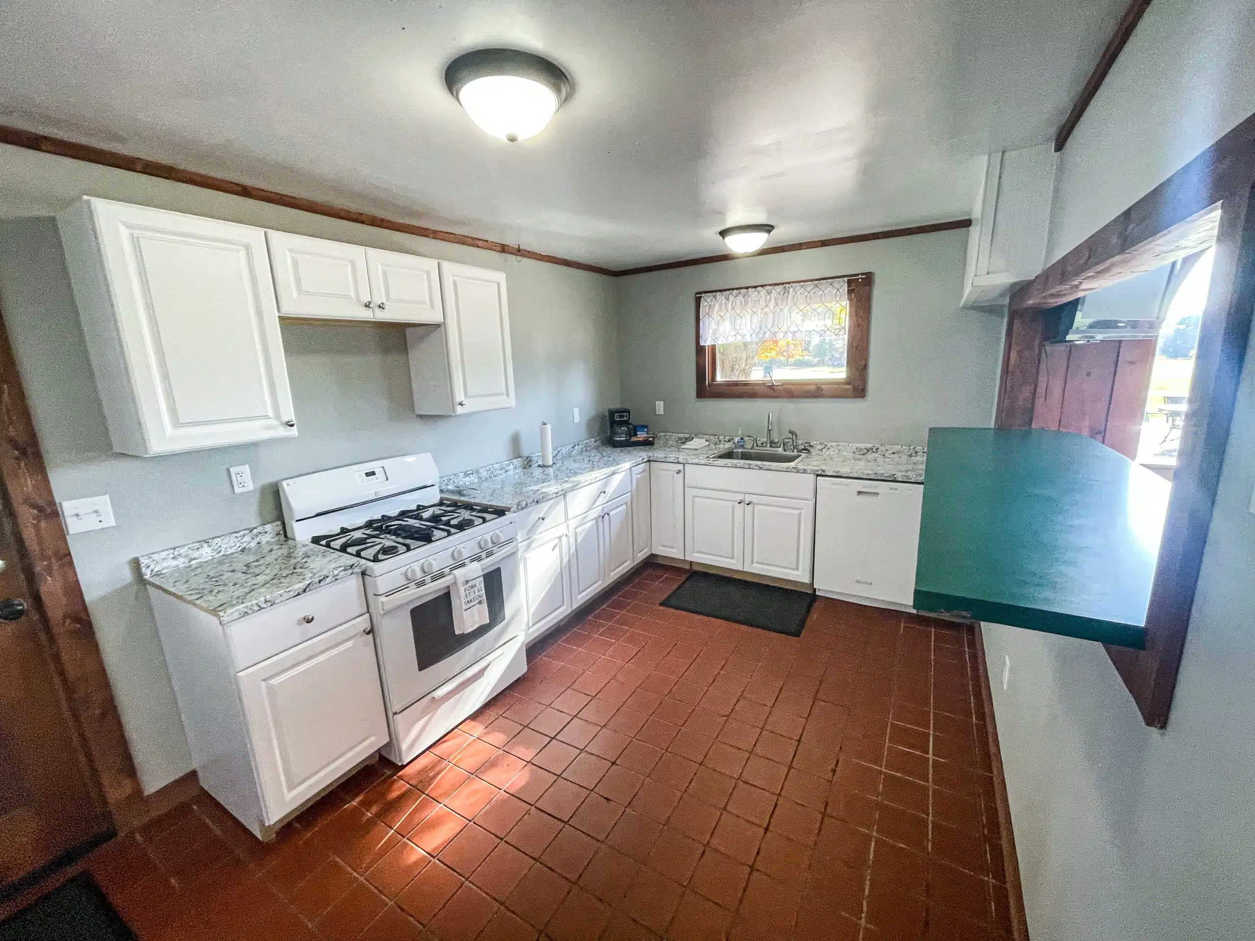 Fully equipped kitchen in the Classic Lodge at Otsego Resort, featuring white cabinetry, granite countertops, gas stove, and a window view of the outdoors.