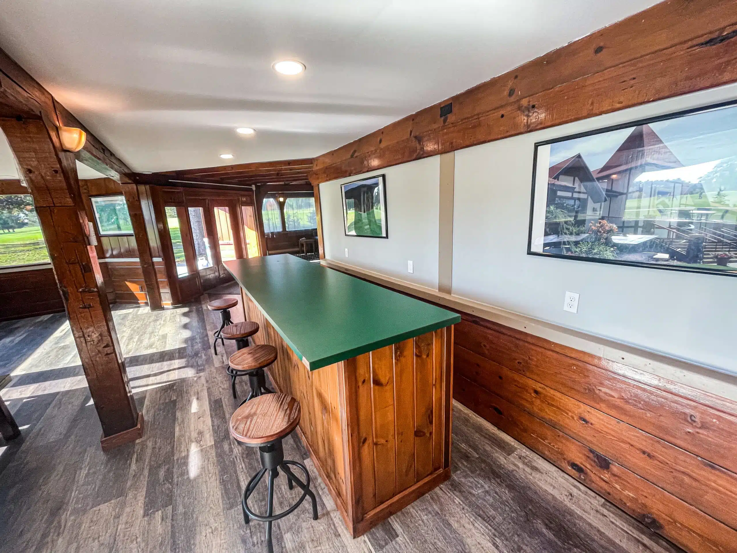 Interior view of the Classic Lodge at Otsego Resort featuring a wooden bar area with green countertop, stools, and large windows showcasing the golf course outside.