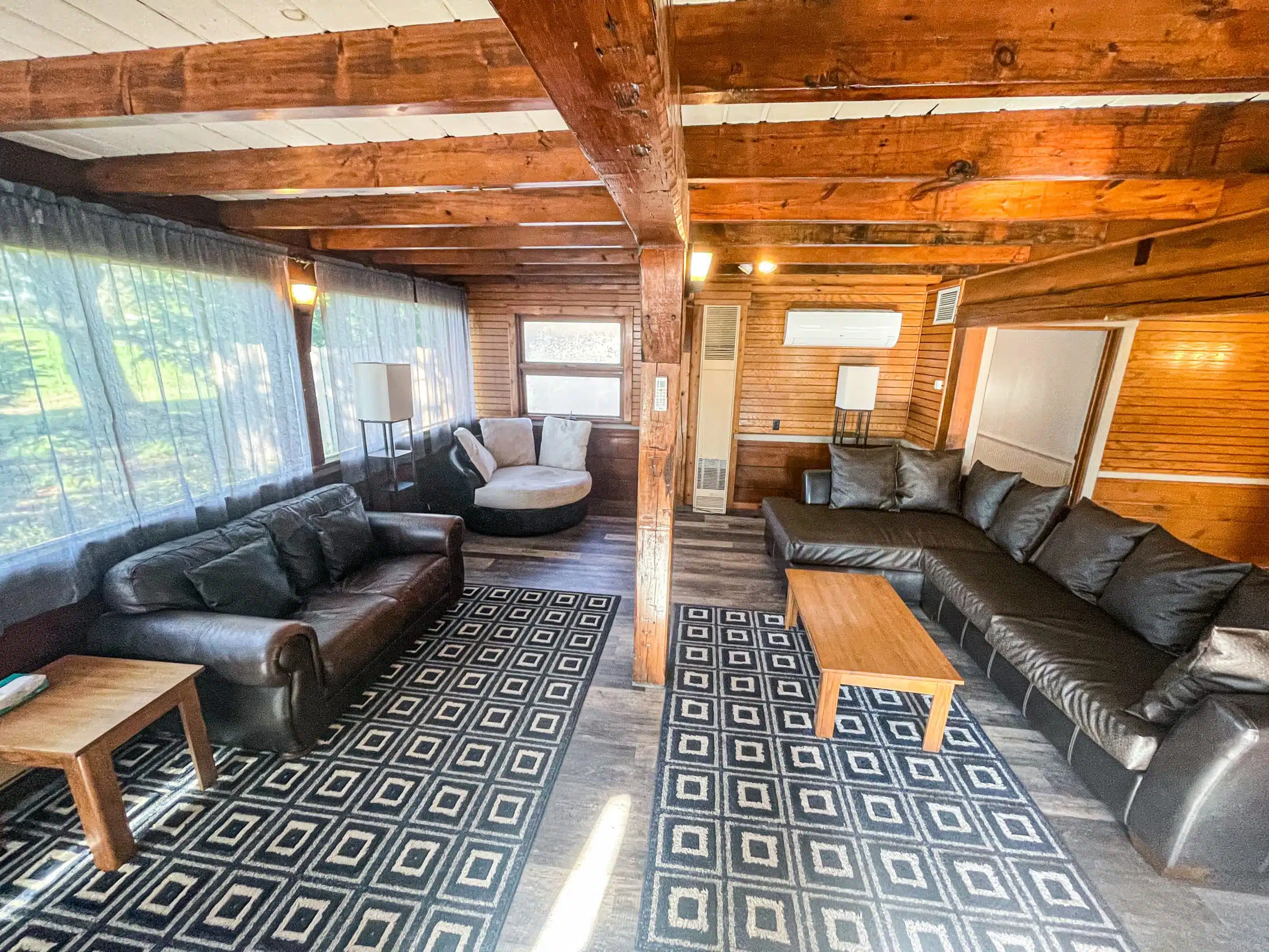 Cozy living room of The Classic Lodge at Otsego Resort featuring leather sofas, a round chair, wooden coffee table, and large windows with sheer curtains, showcasing a rustic design and inviting atmosphere.