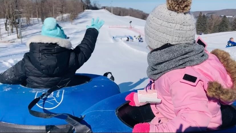 Kids tubing down a snowy hill at Otsego Resort, enjoying winter fun and excitement during the ski competition event.