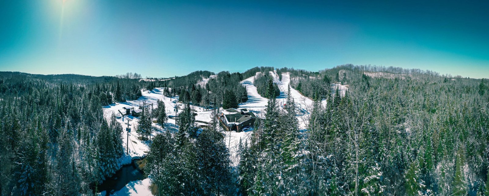 Panoramic view of Otsego Resort's snowy landscape, showcasing ski slopes, evergreen trees, and the Sturgeon River Valley under a clear blue sky.