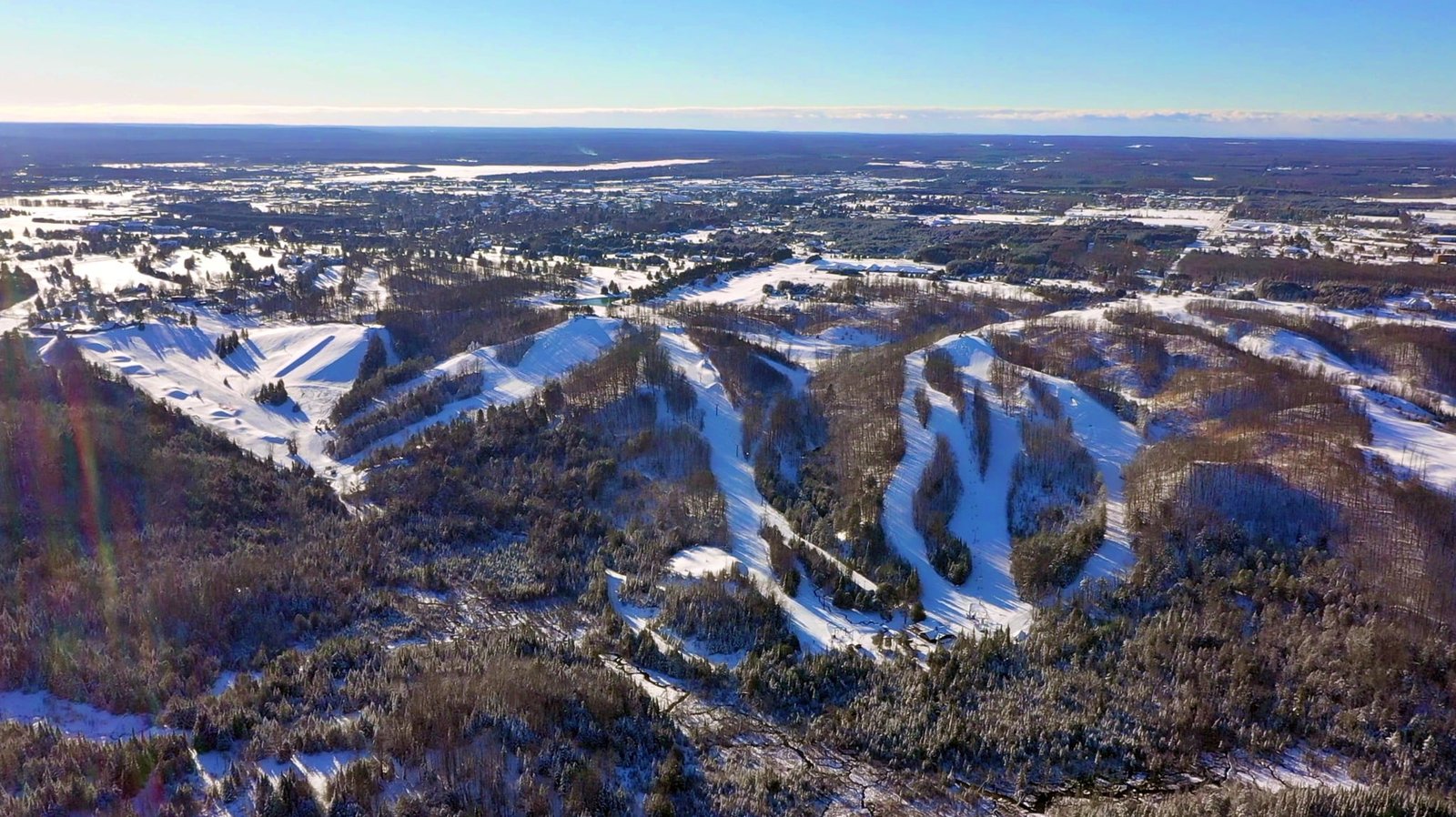 Aerial view of snowy slopes at Otsego Resort, showcasing ski trails and the scenic Sturgeon River Valley under a clear blue sky.