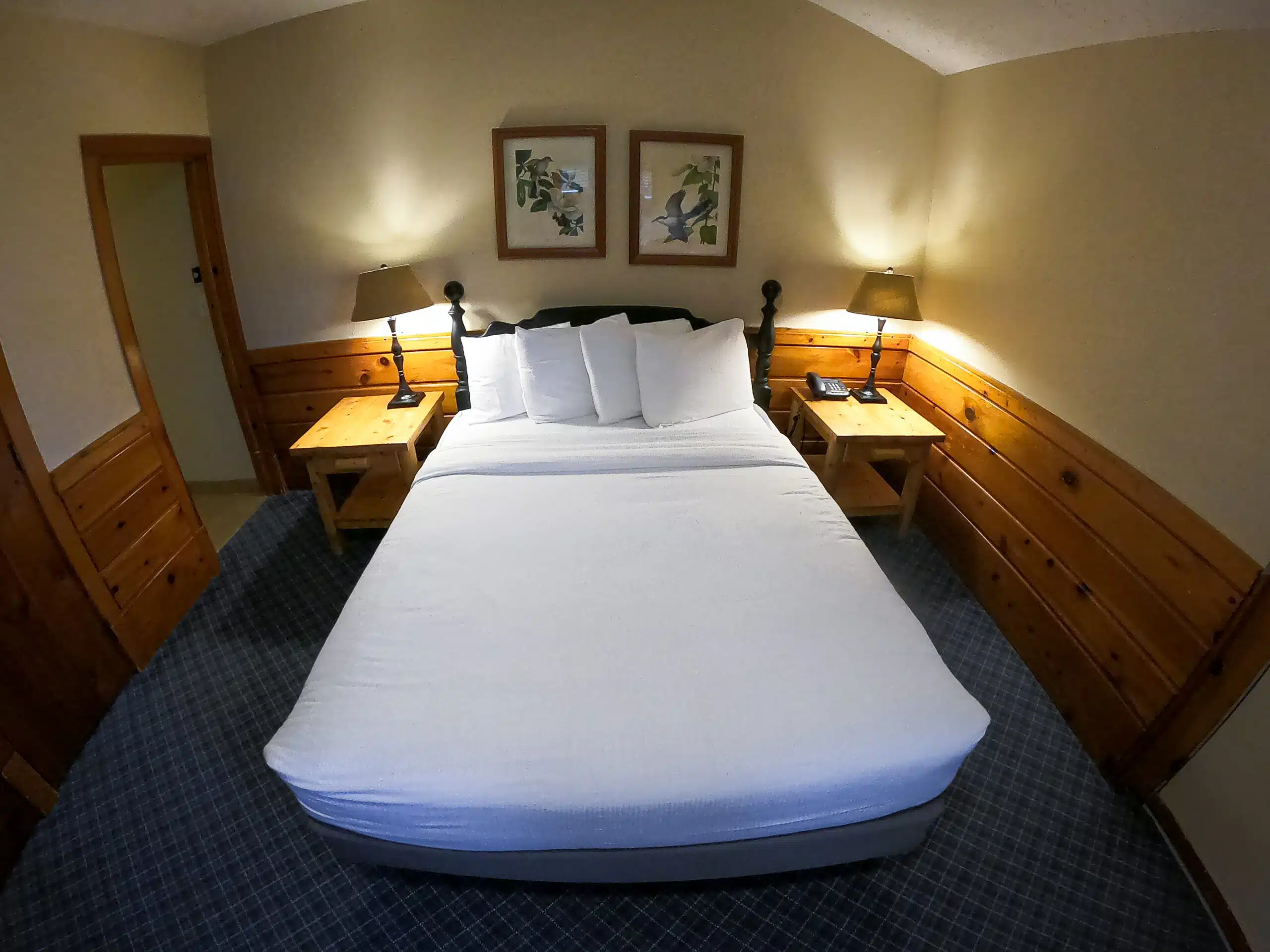 Cozy townhouse bedroom featuring a queen bed with white linens, wooden accent walls, bedside tables with lamps, and framed artwork, ideal for relaxing after mountain activities.
