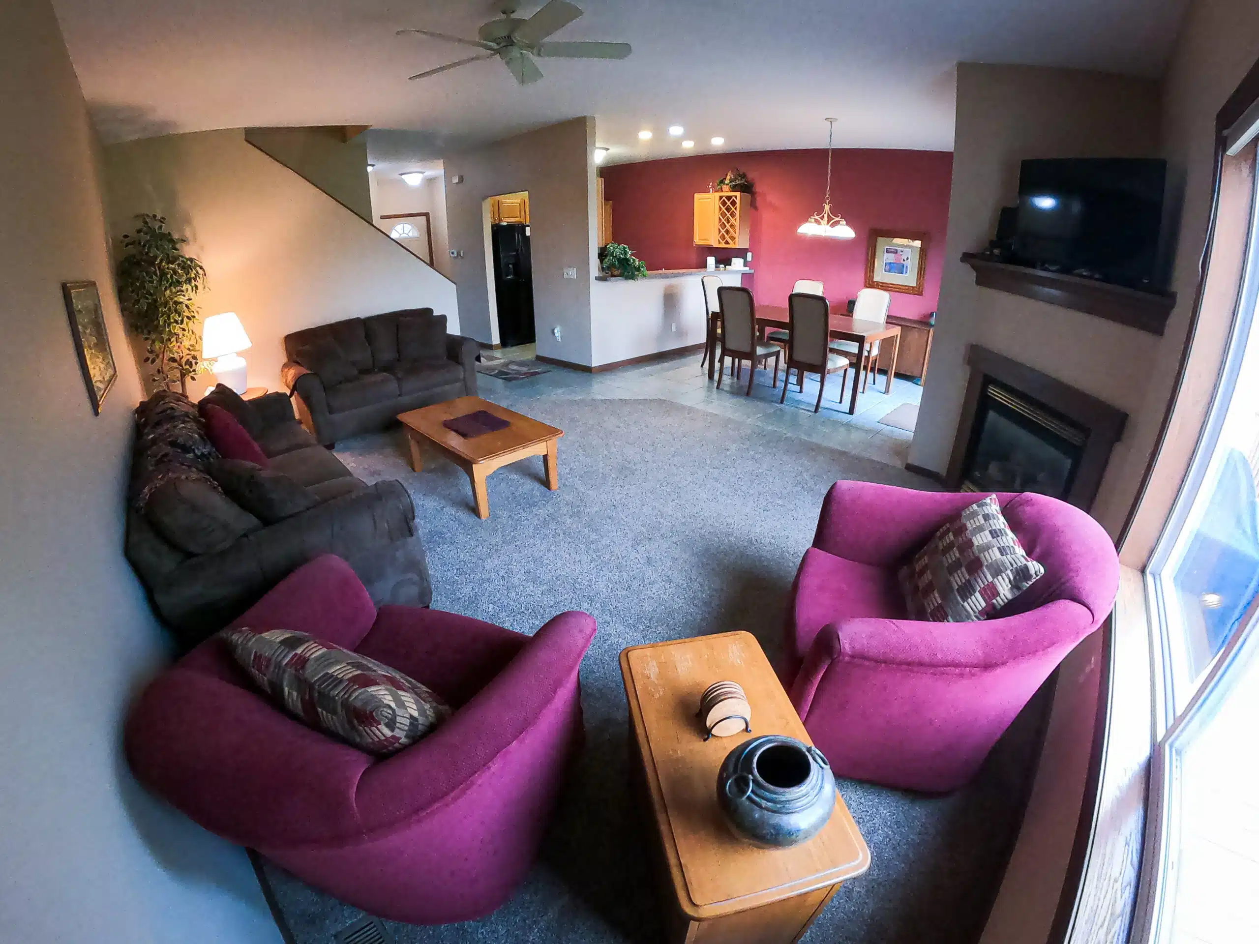 Cozy townhouse living room featuring purple accent chairs, brown sofas, a wooden coffee table, and a dining area, designed for group relaxation after mountain or golf activities at Otsego Resort.