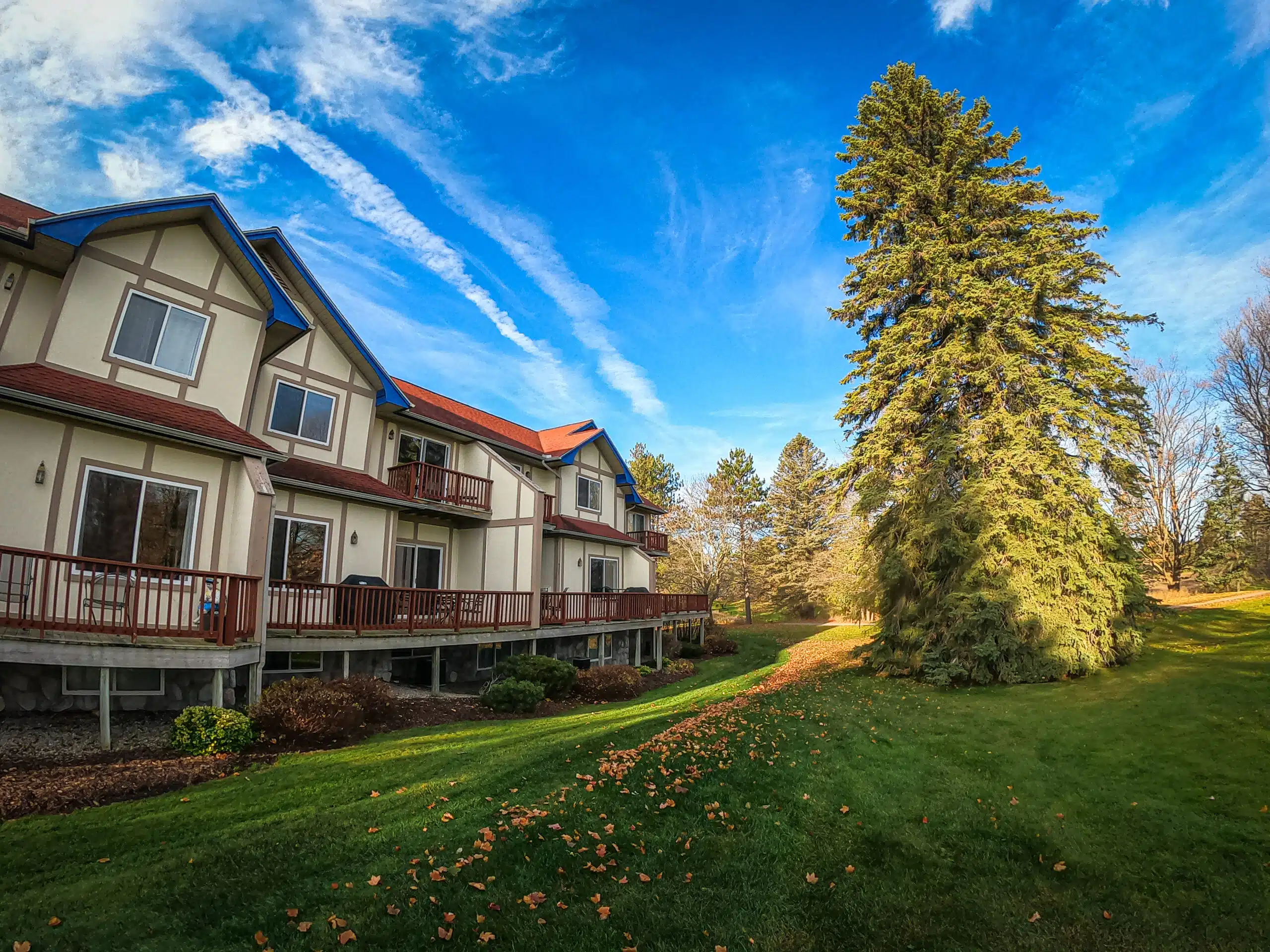Townhouses at Otsego Resort with spacious balconies, vibrant blue roofs, and a lush green lawn, surrounded by trees and a clear blue sky.