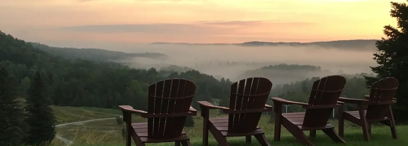 Adirondack chairs overlooking a misty valley at sunset, capturing the serene alpine setting of Otsego Resort, ideal for wedding ceremonies and memorable moments.