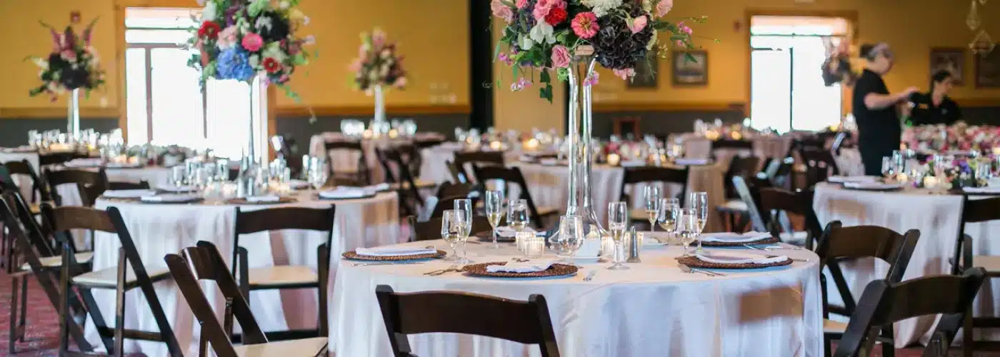 Elegant wedding reception setup at Otsego Resort featuring round tables adorned with floral centerpieces, glassware, and white linens, highlighting the venue's charming atmosphere for celebrations.