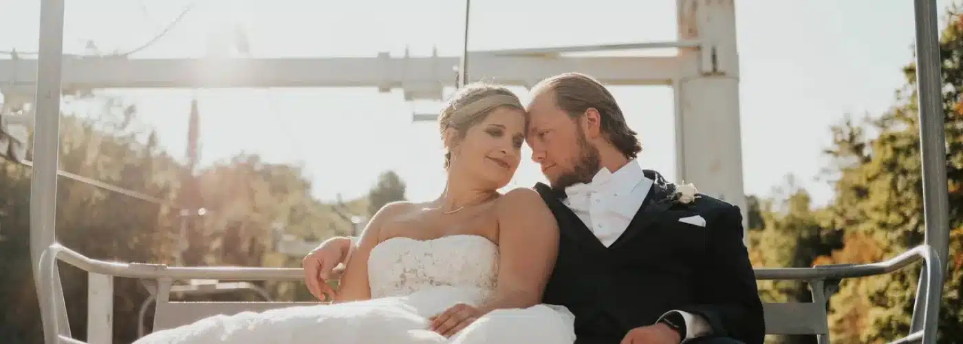 Bride and groom sharing a romantic moment on a ski lift, surrounded by lush greenery, symbolizing love and celebration at Otsego Resort weddings.