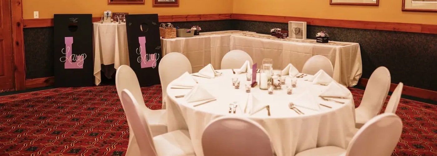 Reception setup in Otsego Resort's intimate Pontresina room, featuring a round table with white linens, elegant table settings, and decorative signs, creating a warm atmosphere for weddings and events.