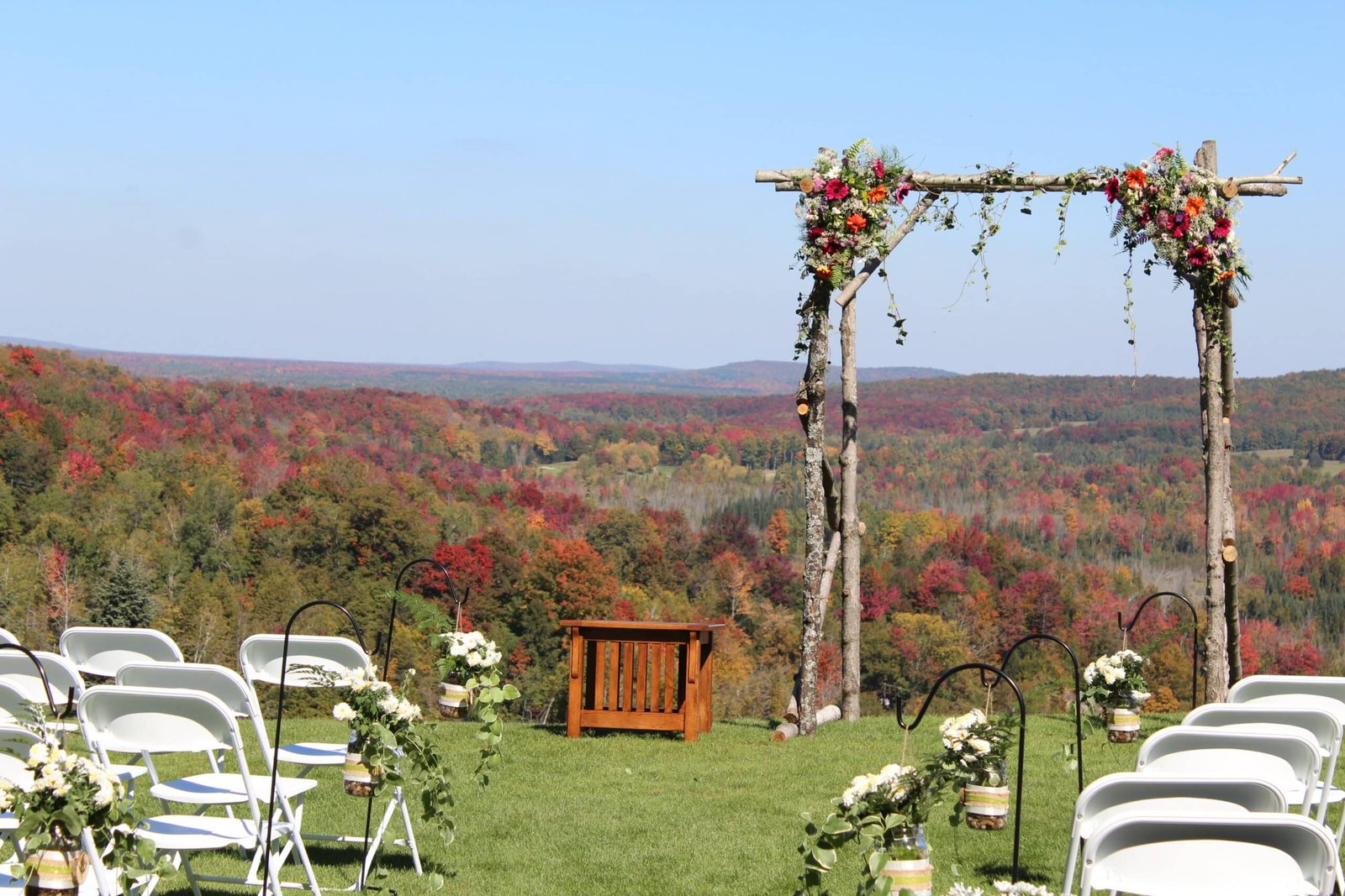 Wedding altar adorned with flowers, overlooking vibrant fall foliage in the Sturgeon River Valley, with white chairs arranged for guests.