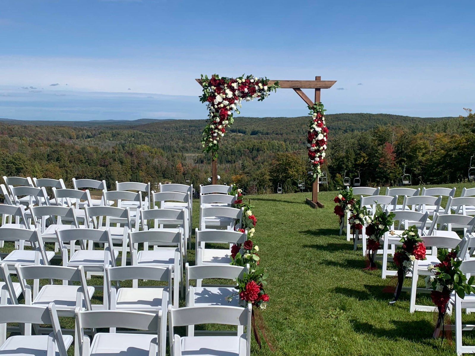 Wedding altar adorned with flowers, surrounded by white chairs, overlooking the scenic Sturgeon River Valley at Otsego Resort.